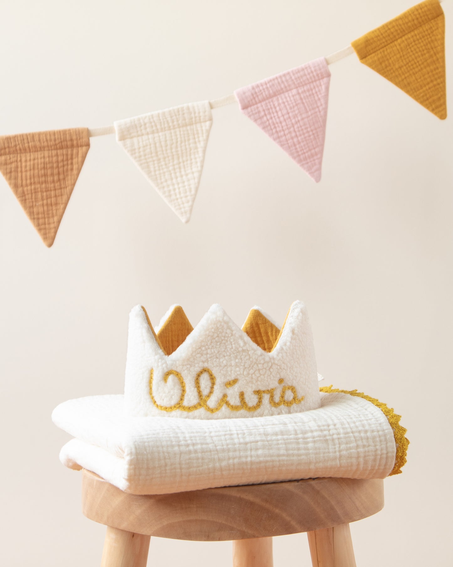 coroa de aniversário reversível em pelo carneirinho bege com nome bordado à mão, grinalda de bandeirolas tecido colorida